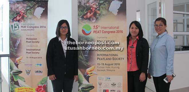 Lulie (right) and the IPC secretariat standing next to posters with details of the congress at the Tropical Peat Research Laboratory.