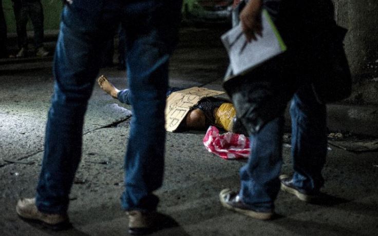 Philippine police examine the body of an alleged drug dealer -- his face covered with packing tape and a placard reading "I'm a pusher" -- who was shot dead in Manila, on July 8, 2016. Photo by AFP