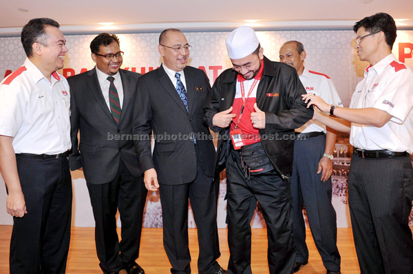 Jailani (third left) looks on as a Pos Malaysia staff dons a duty jacket signifying work during the haj season. Also present is Shukrie (right) and other official directors from Pos Malaysia and DRB-Hicom Bhd. — Bernama photo 