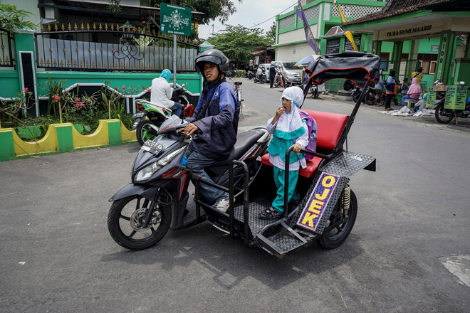 Hartanto, a disabled motorcycle taxi driver, carries a student passenger in Yogyakarta, Indonesia. — Reuters photo