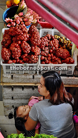 A local woman keeps an eye on two baskets of asam paya while holding her sleeping child. 