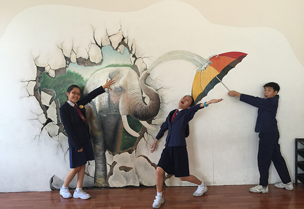 (from left) Emanuelle, Shana and Joshua having a light moment while posing next to their school’s 3D art wall. 