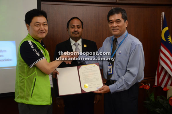 Joon (left) presents the MoU to Dr Chin (right). Looking on is Dr Hariskrihna.