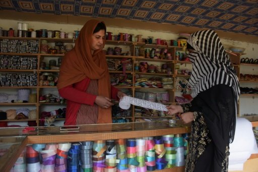 Pakistani Kashmiri Sara Rasheed (L) sells border trim cloth to a customer at her shop in the women's market on the outskirts of the town of Rawalakot. - AFP/Sajjad Qayyum