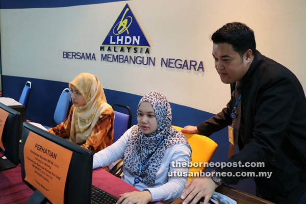 TELITI: Shahminan (kanan) ketika meneliti proses kemas kini secara online yang dilakukan                            di pejabat LHDN Cawangan Kuching.