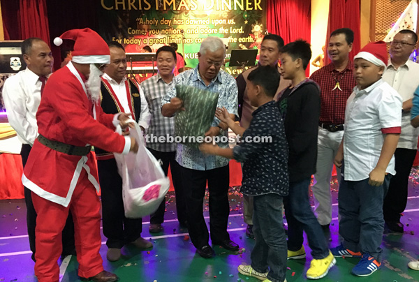 Manyin (centre) presents a gift from the organisers to these children. From right are Dahim, Ik Pahon, John, Father Jerome Juleng, Henry and Boniface.