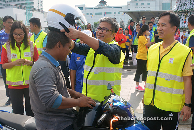 Dr Annuar (second right) helps a motorcyclist put on his new helmet during the road safety campaign for Christmas at Sibu Town Square yesterday. He is flanked by Davina and Hii (right). 