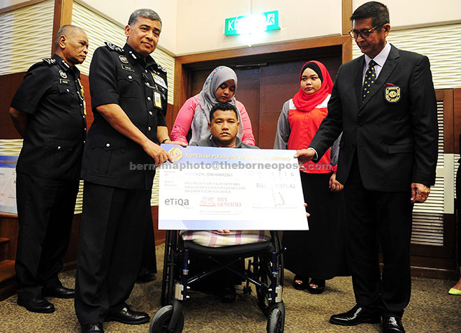 Khalid (second left) presents insurance payout to a cooperative member, Lance Corporal Nur Faizal Hamzah (centre) who lost both his legs in an accident on Mac 13 at an event at Bukit Aman police headquarters. — Bernama photo