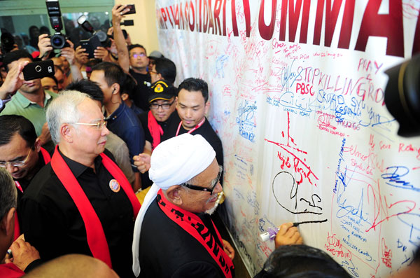 Najib (left) witnesses PAS president Datuk Seri Abdul Hadi Awang signing a poster to show support during the Solidarity for Rohingyas gathering at Stadium Titiwangsa. — Bernama photo