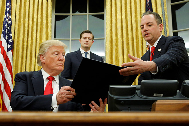 Trump hands Chief of Staff Reince Priebus (right) an executive order that directs agencies to ease the burden of Obamacare, after signing it in the Oval Office in Washington. Also pictured is White House Staff Secretary Rob Porter (behind). — Reuters photo