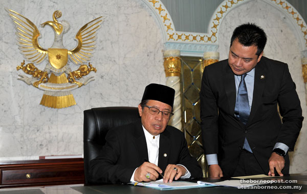 Abang Johari signs a document to mark his first day at the Chief Minister’s Office, witnessed by Wan Khalik.