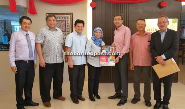 Sia (third right) handing over a promotional poster to Nancy, while Yong (third left) and other Rotarians look on. 