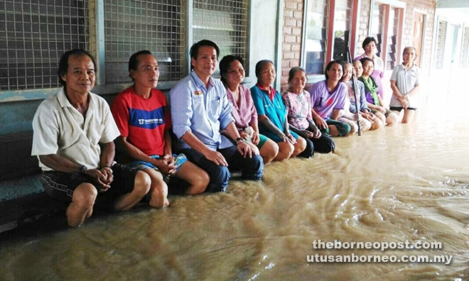 Dennis (third left) sits with residents of Long Wat in the knee-deep flood water at the Ruai of their longhouse.