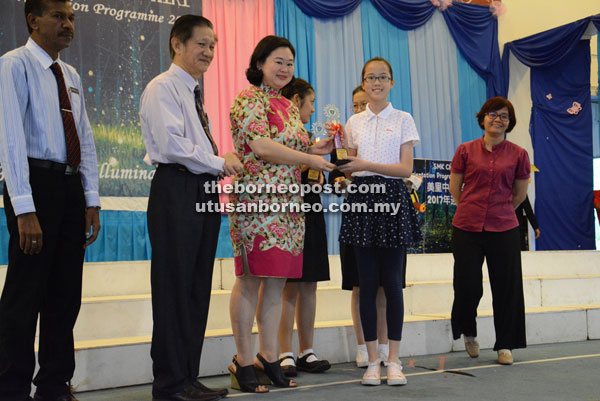 Rita Ting, representing Tan Sri Datuk Paduka Chai Yu Lan, presents a trophy to an excellent student.