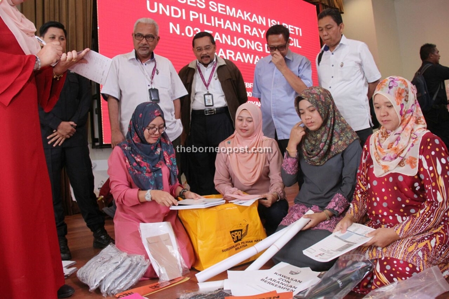 Presiding officers of the Tanjong Datu by-election make a checklist of the equipment and materials needed for polling tomorrow while EC chairman Datuk Seri Mohd Hashim Abdullah (standing, fourth right) looks on.