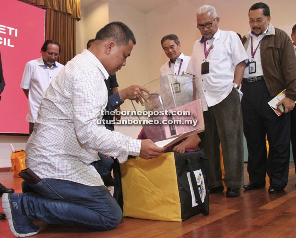 Nasri (left) goes through the checklist of items in the EC polling bag before heading off  to SK Telok Melano, as Mohd Hisham (second right) looks on. 