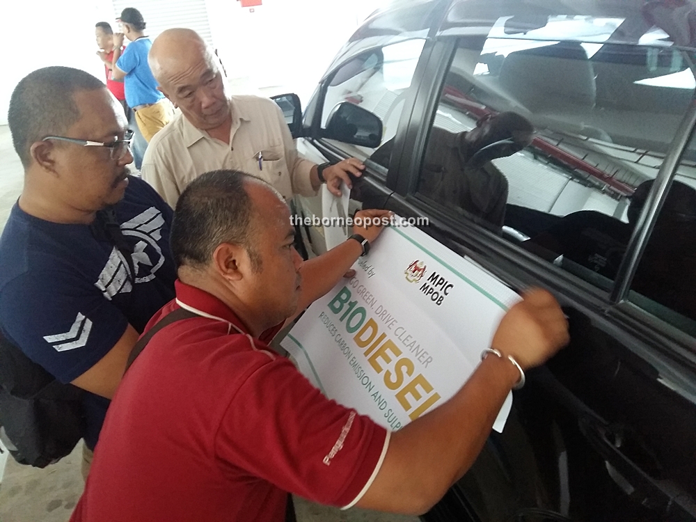 Malaysian Palm Oil Board (MPOB) staff placing event liveries on a participating vehicle as part of their final preparations before the start of the expedition.