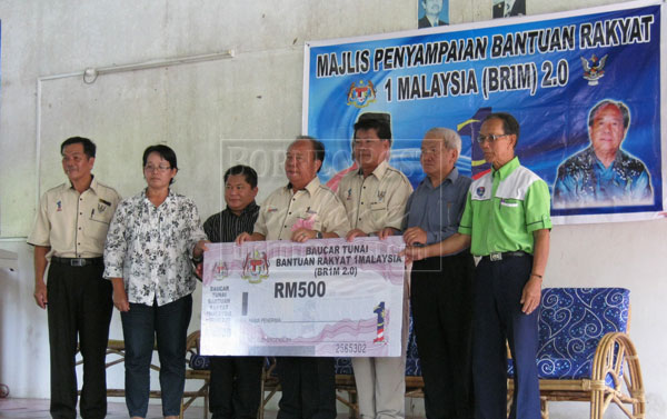 PEOPLE’S AID: Henry (centre) hands over a BR1M2.0 mock voucher to mark the distribution. 