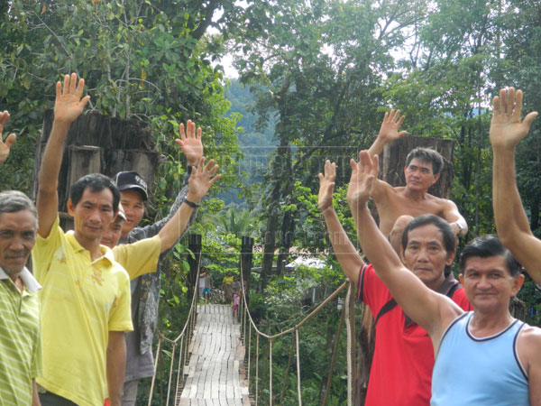 SATISFYING: Goh (right) and Alah (second right) posing for a picture with village folk in front of the hanging bridge.