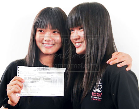 DOUBLE JOY: (From left) Lih Bin shows her 12A+ result while her twin sister Lih Wen looks on.