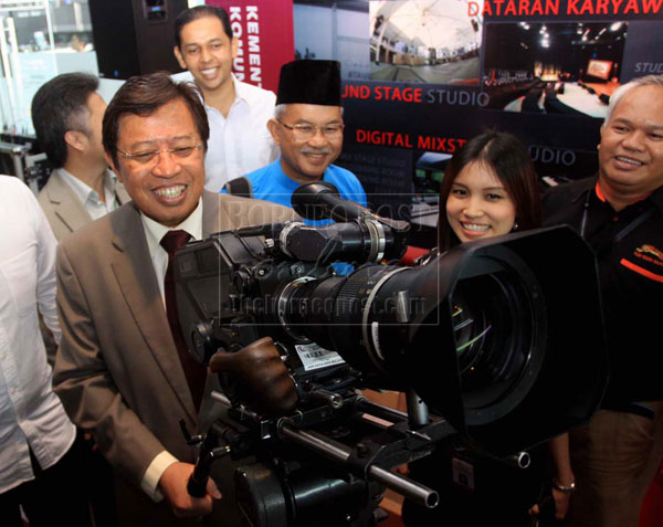 HANDS ON EXPERIENCE: Abang Johari trying his hands on a film equipment on display at one of the exhibition booths. On his left is Assistant Minister of Tourism Datuk Talib Zulpilip.