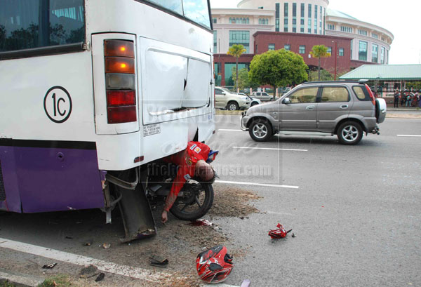 The victim's body pinned between his motorcycle and the undercarriage of the bus at Jalan Sulaiman yesterday.