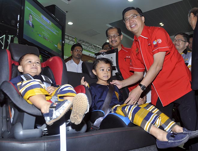 Liow fastens the seat belt for a child during the campaign. — Bernama photo