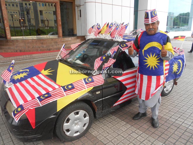 Azahari is seen in his flag outfit next to his flag-covered car. 