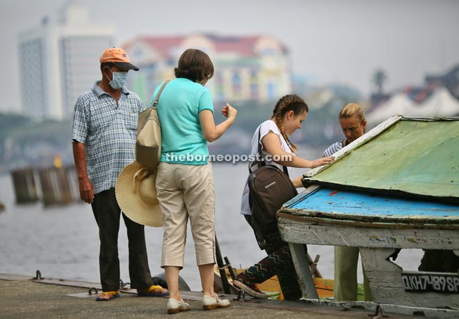 A ‘perahu tambang’ operator, wearing a mask, waits patiently as tourists board his boat at Pangkalan Sapi in Petra Jaya, Kuching, yesterday. Haze has returned, and the API reading in Kuching was 103 as of 2pm yesterday. — Photo by Muhammad Rais Sanusi