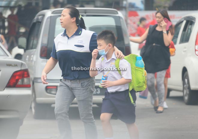 An adult guides a young boy wearing facemask while crossing a busy street in Kuching.