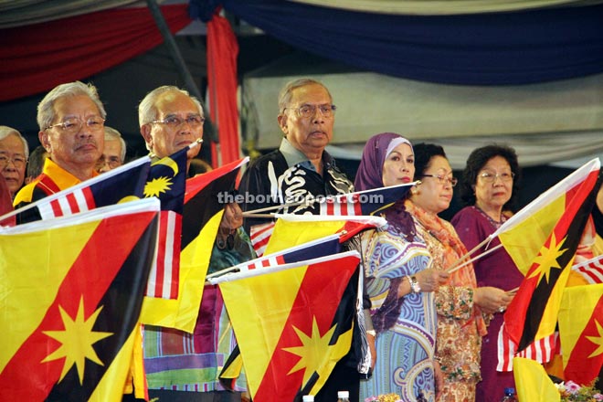 Jabu (second left), together with Adenan (centre) and Land Development Minister Tan Sri Datuk Amar Dr James Masing (left), waves the Malaysia and Sarawak flags during the airing of the Jalur Gemilang song. Also seen are (from fourth left) Jamilah and Jabu’s wife Dato Sri Empiang.  