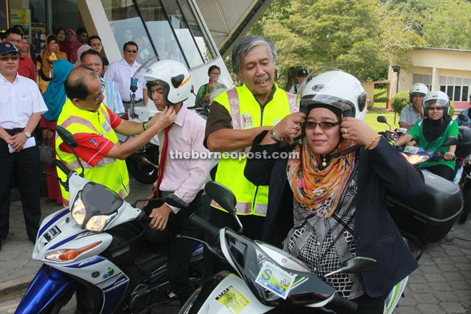 Abdul Ghafar (left) and Bedui (second right) put helmets on participants of the Road Safety Awareness Programme. — Photo by Jeffrey Mostapa