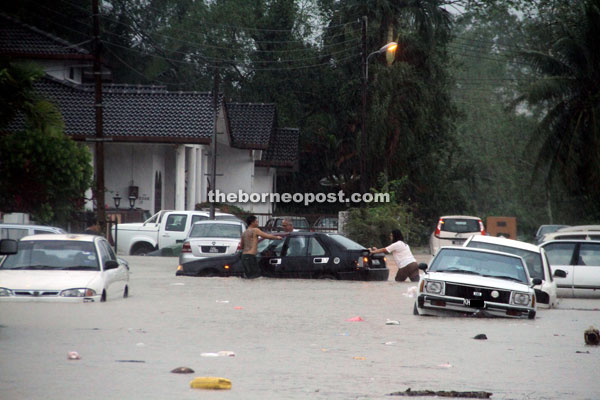 Kampung Tabuan Dayak residents attempt to save a vehicle from the flood waters. — Photo by Chimon Upon