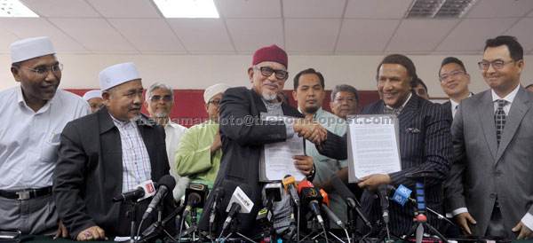 Abdul Hadi (centre) shaking hands with Abdul Kadir marking the establishment of a pact between both parties at the media conference in Kuala Lumpur yesterday. — Bernama photo 