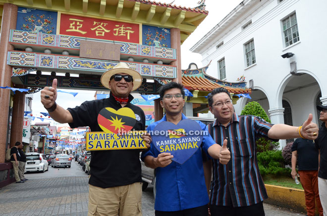 Nazri (left), Pau and Wee (right) with a ‘Kamek Sayang Sarawak’ placard in front of the Carpenter Street Arch in Kuching. — Photo by Jeffery Mostapa