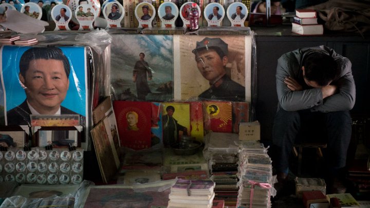 A vendor takes a nap next to posters showing the late Chinese chairman Mao Zedong and Chinese President Xi Jinping at a market in Beijing on May 15, 2016. Photo by AFP