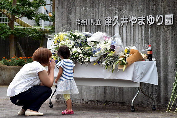 A mother and her daughter offer flowers for the victims of a knife rampage at the main entrance to the Tsukui Yamayuri En care centre in Sagamihara, Kanagawa prefecture on July 28. – AFP photo