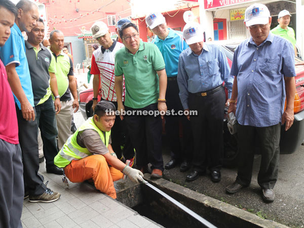 Abang Wahap (fifth right), with Wee on his left, observes a worker scale a drain that has grease build-up at Carpenter Street. 