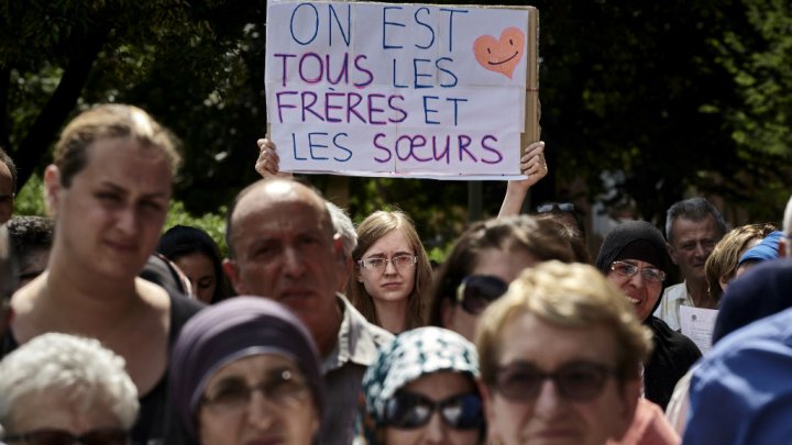 A woman holds a placard reading "We are all brothers and sisters" as she takes part in a silent march on July 30, 2016 in Lyon following the attack on a church in Saint-Etienne-du-Rouvray on July 26. Photo by AFP