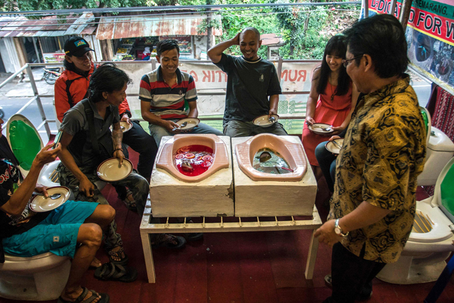 Photo shows customers having a meal at the ‘Jamban Cafe’ in the city of Semarang on Java island, a small eatery where a handful of diners sit on upright toilets around a table where food is served in two squat toilets. — AFP photo