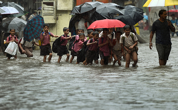Indian school children walk along a flooded street during heavy rain showers in Mumbai on Aug 5. — AFP Photo