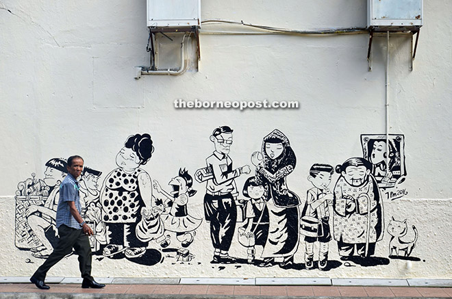 A man walks pass a mural painting which depicts the three major races in Sibu.