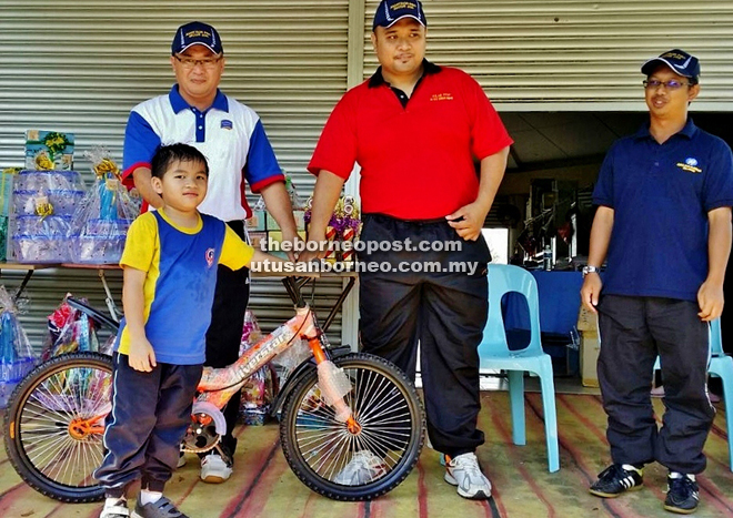 Mohd Fitri (centre) hands over a prize in the form of a bicycle to a boy, who collected more than RM500 for the joggerthon.