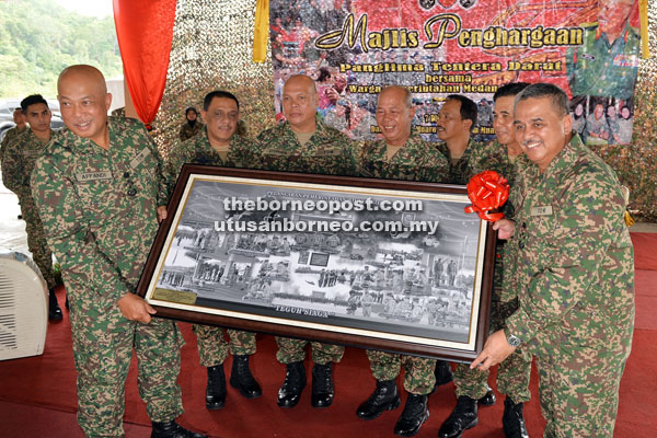 Raja Mohamed (left), assisted by Mohd Zaki (right) shows the memento presented to him  at his appreciation event organised by the East Field Command at Muara Tuang Camp in Kota Samarahan.